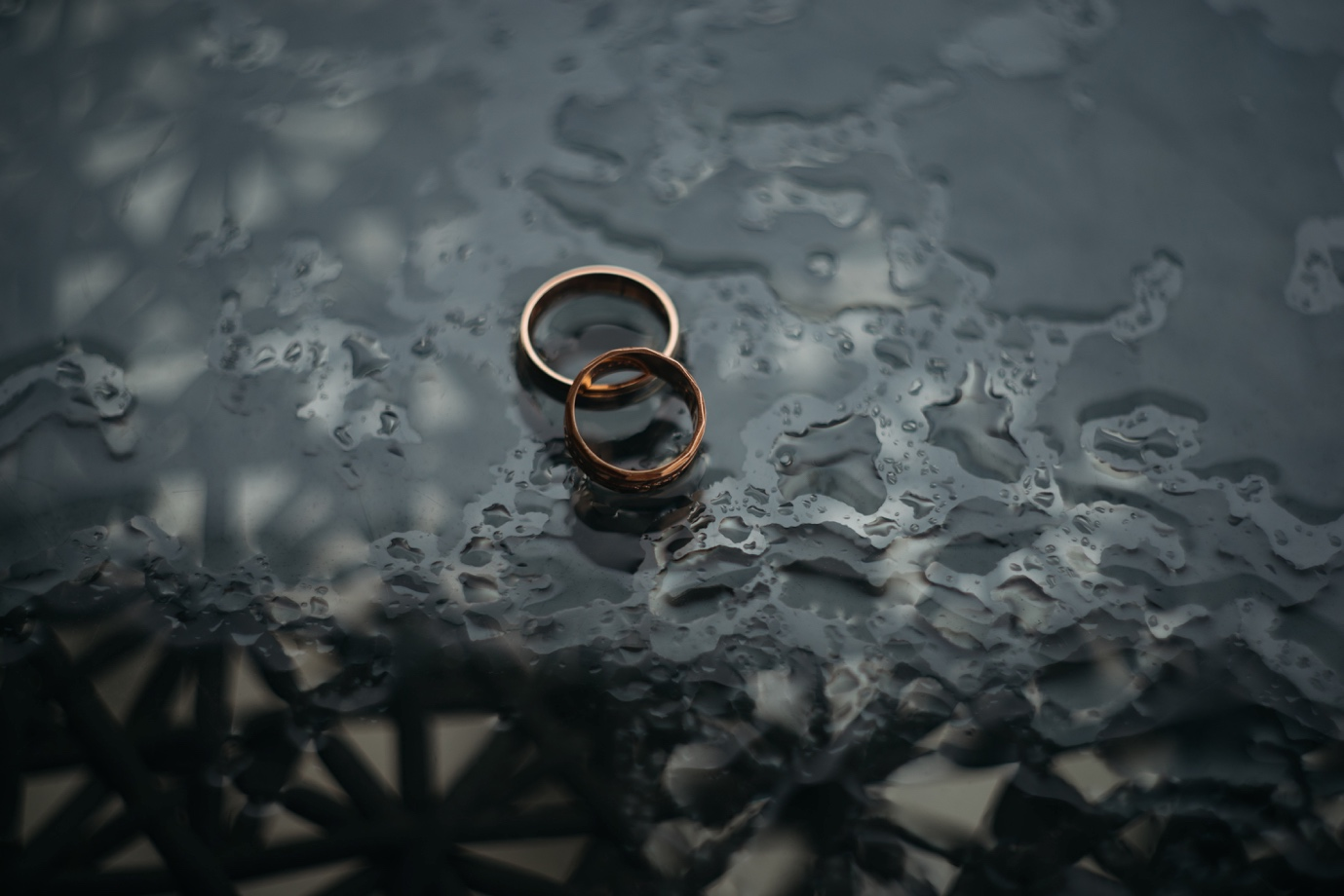 Two wedding rings on a glass table with rain water