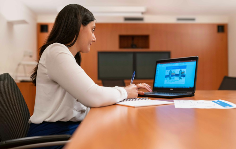 An image of a woman using her laptop while writing something down