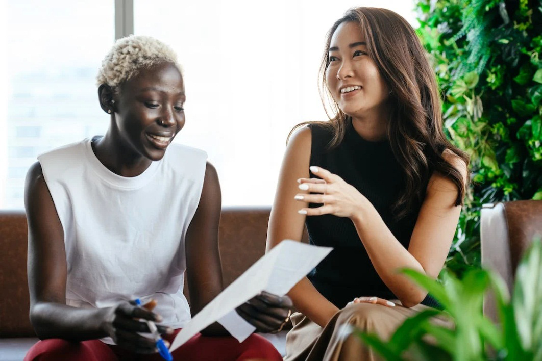 An image of two women smiling while talking and looking at a document 