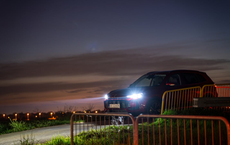 A red SUV with headlights on is parked along a rural road at sunset