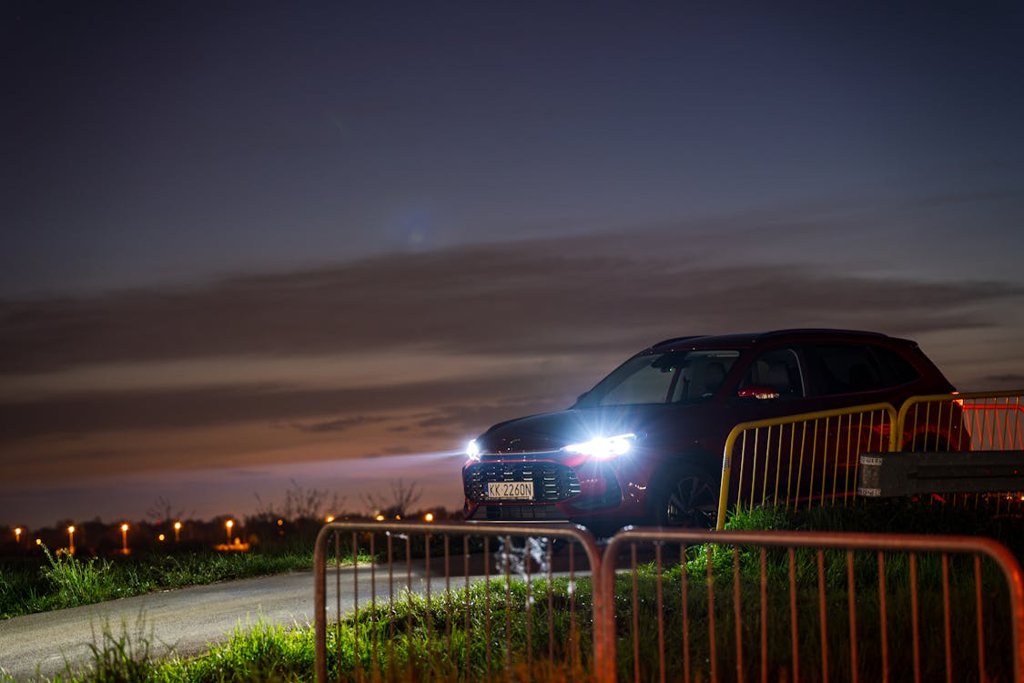 A red SUV with headlights on parked along a rural road at sunset