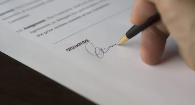 A hand signs a document with a pen