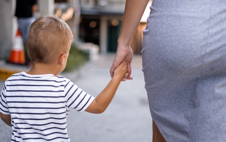 a child holding his mother's hand, walking down the street