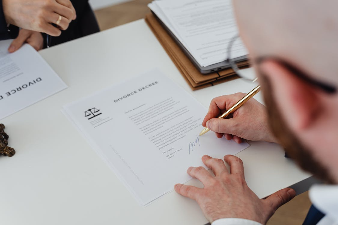 Over the shoulder shot of divorce papers being signed by a person. Over the shoulder shot of divorce papers being signed by a person.
