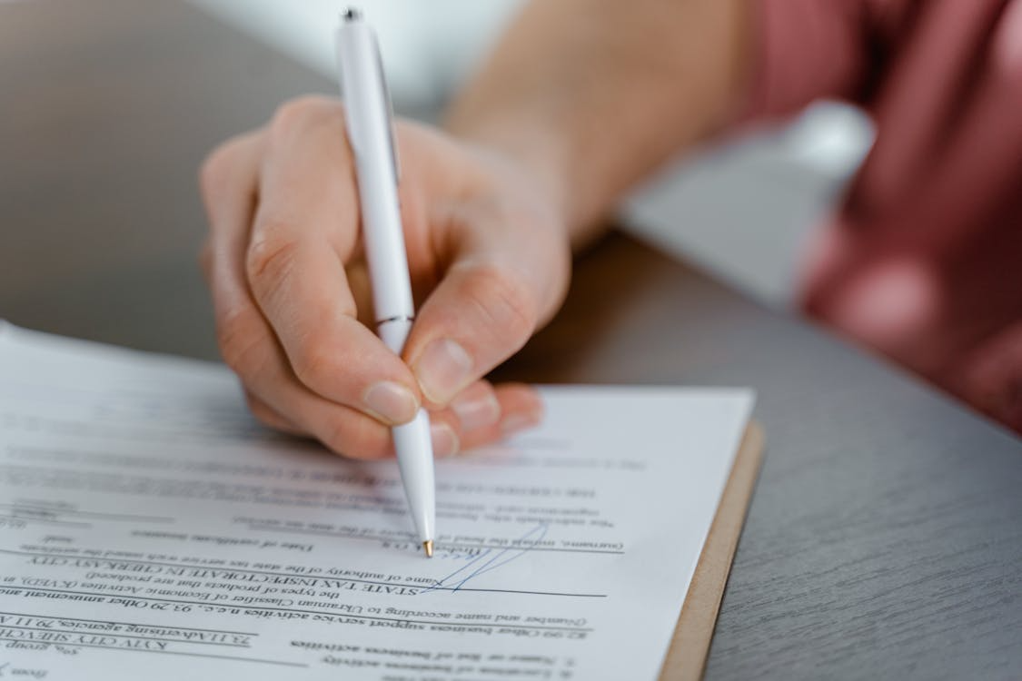close-up of a person holding a white pen signing a document close-up of a person holding a white pen signing a document