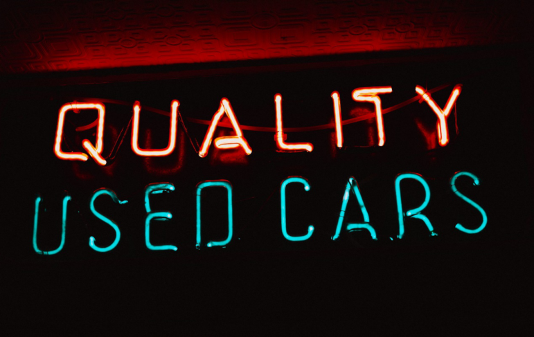 A neon sign promoting available used cars.